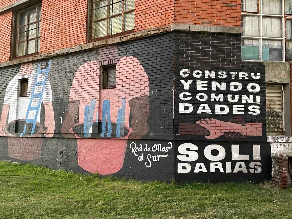 Large mural of people holding large pots of soup with text that says "constructing solidarity community".